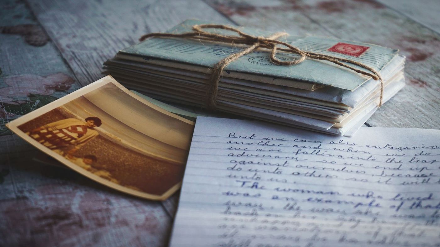 Bundle of vintage letters, an old photograph, and a handwritten note on a wood table, representing sorting through a loved one's keepsakes during a Canyon Count