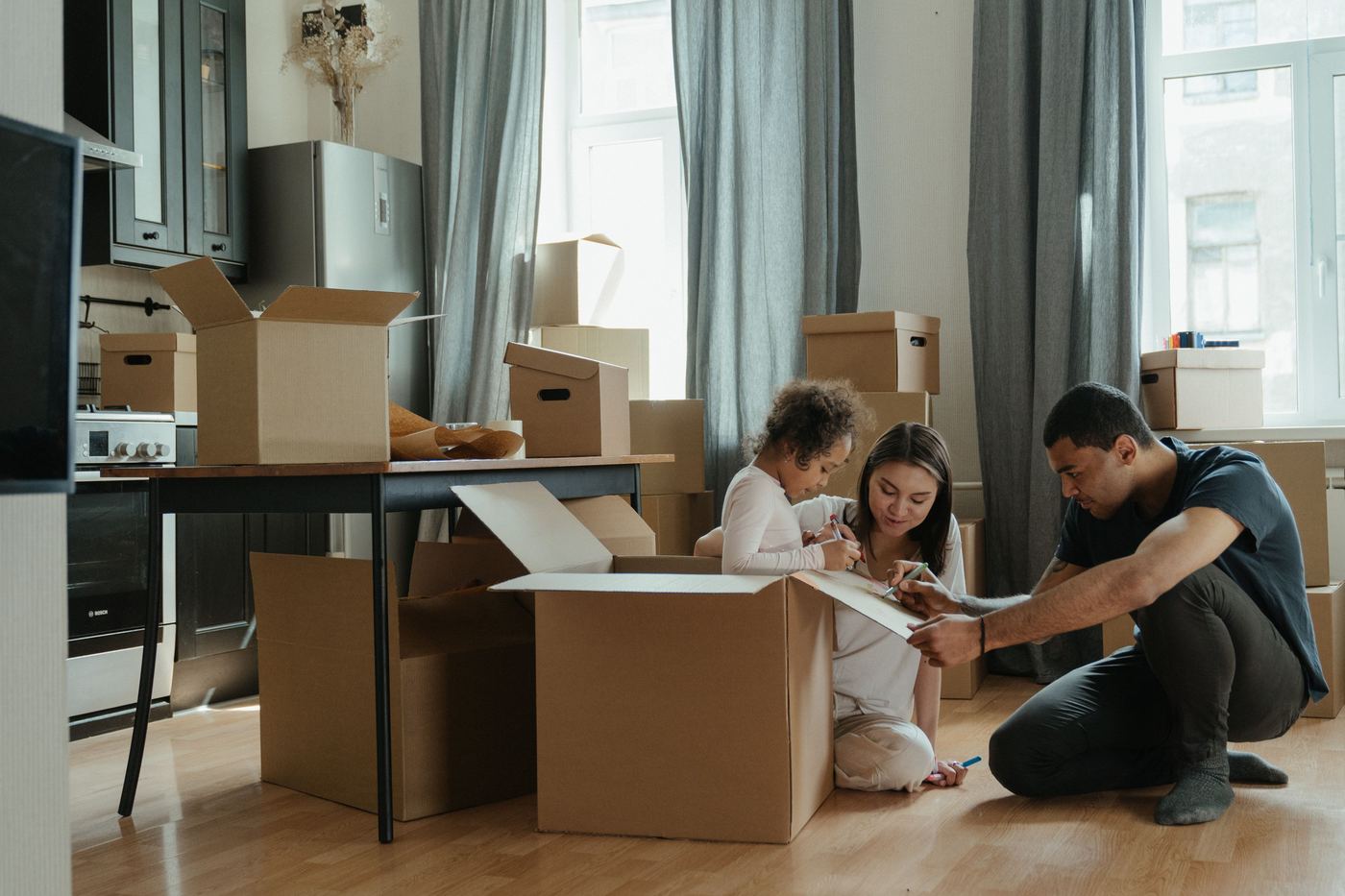 A family sitting together on the floor of their new home, unpacking moving boxes surrounded by plants and natural light
