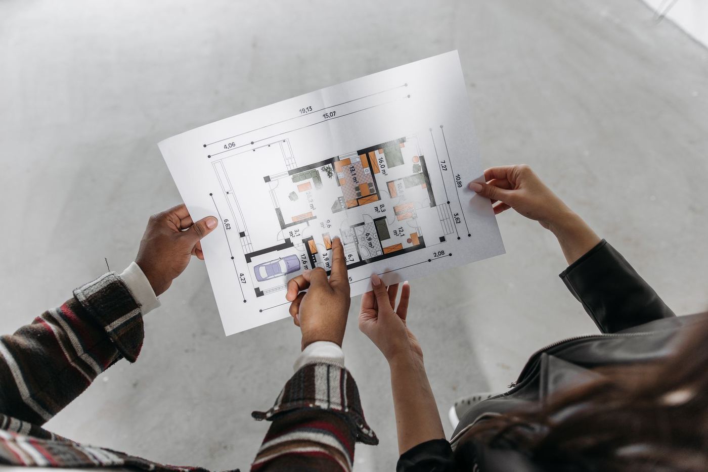 Two hands hold an architectural floor plan at a new construction home site with a concrete floor and framing in the background