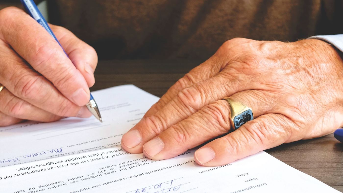 Close-up of hands signing estate paperwork at a desk, representing settling a probate or inherited property sale