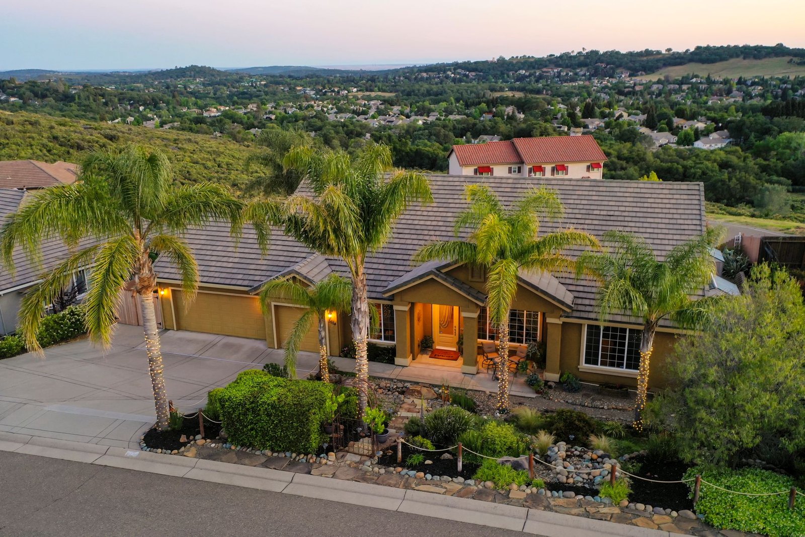 A hillside home in the valley at dusk, palms lit along the driveway
