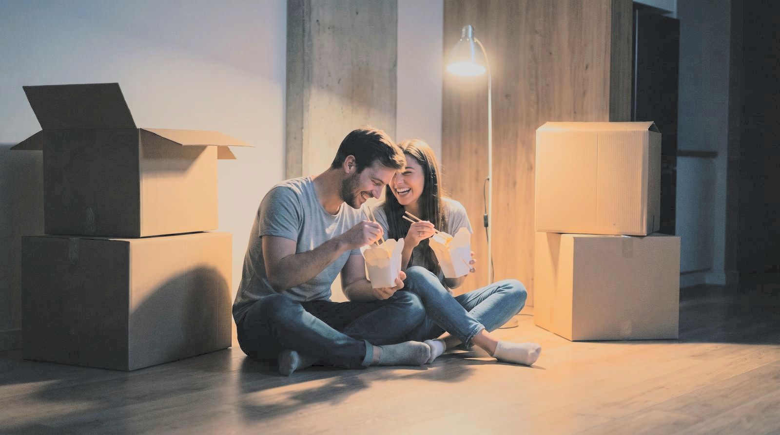A young couple eating takeout on the floor of their empty new living room